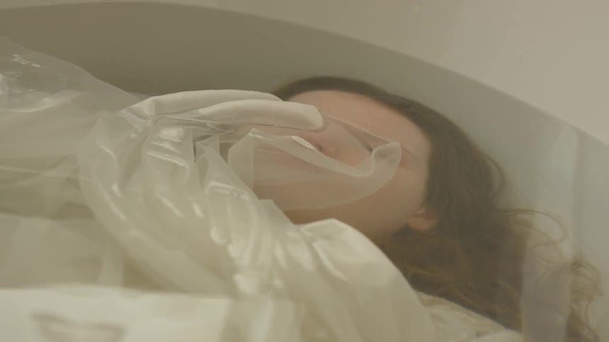 A white woman lies submerged under water in a bathtub