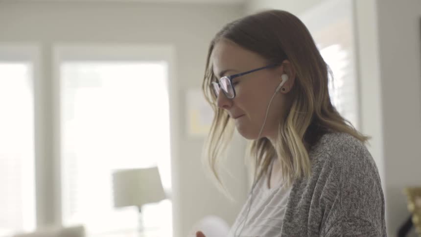A woman wearing earbuds sways and bops her head while listening to music
