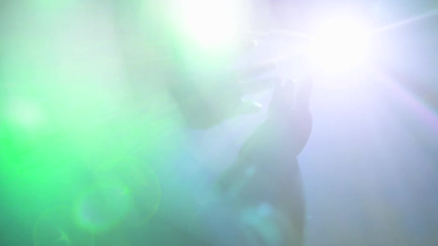 A person is turning their wrists with their hands stretched out while looking at a stage light