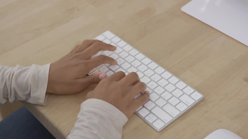 A person is typing on a wireless white keyboard