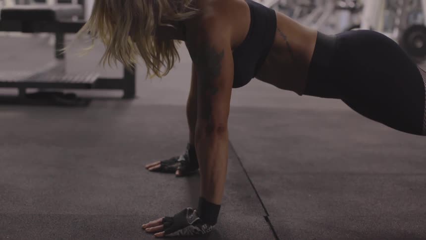 A woman in a sports bra does push ups at a gym