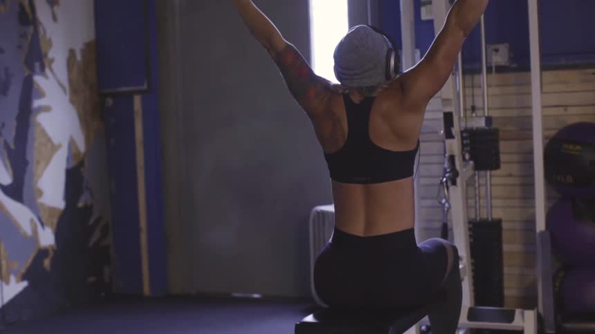 Blonde female wearing a beanie and headphones doing a chest press workout at the gym