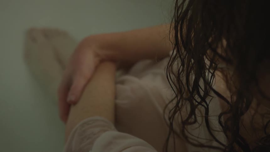 A white woman sits hunched over in the bathtub