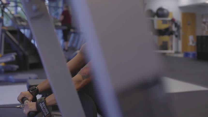 A white woman smiles as she exercises with a rowing machine at the gym