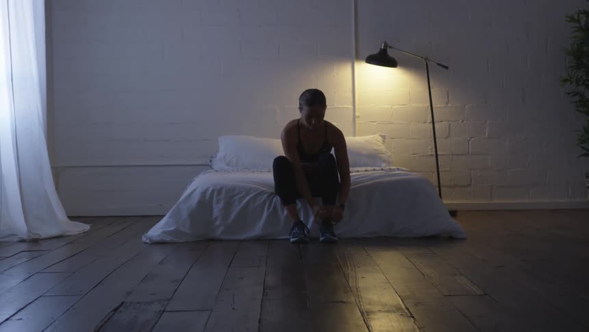 Woman sits on the end of the bed and ties her shoe laces