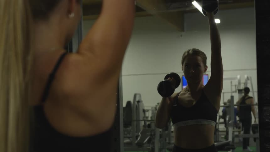 Woman lifting weights in front of mirror on a gym