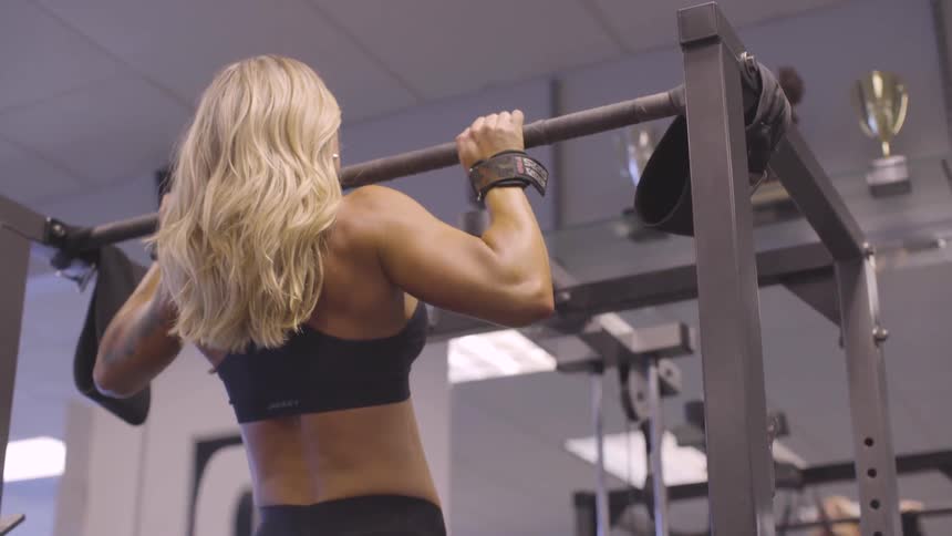 A tanned white woman does chin ups in a gym