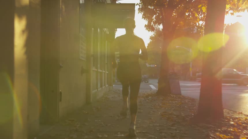 Young woman in athletic wear running on city sidewalk in sunlight