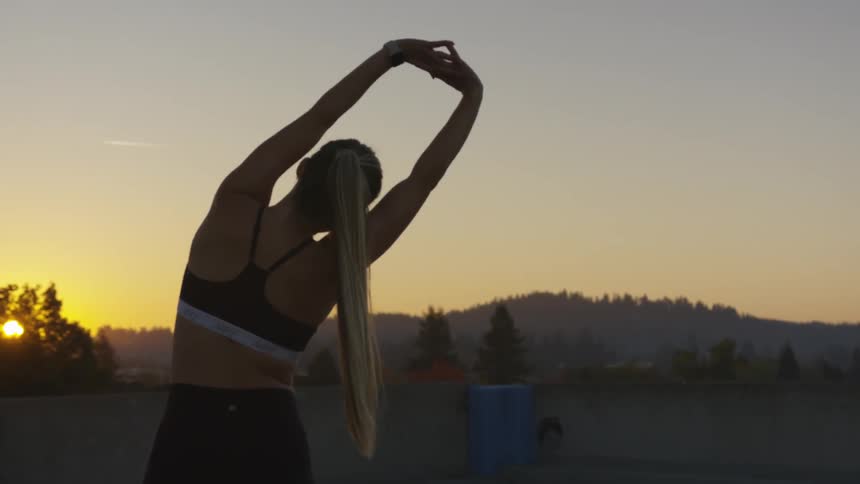 Woman warming up for exercises on a roof during sunset