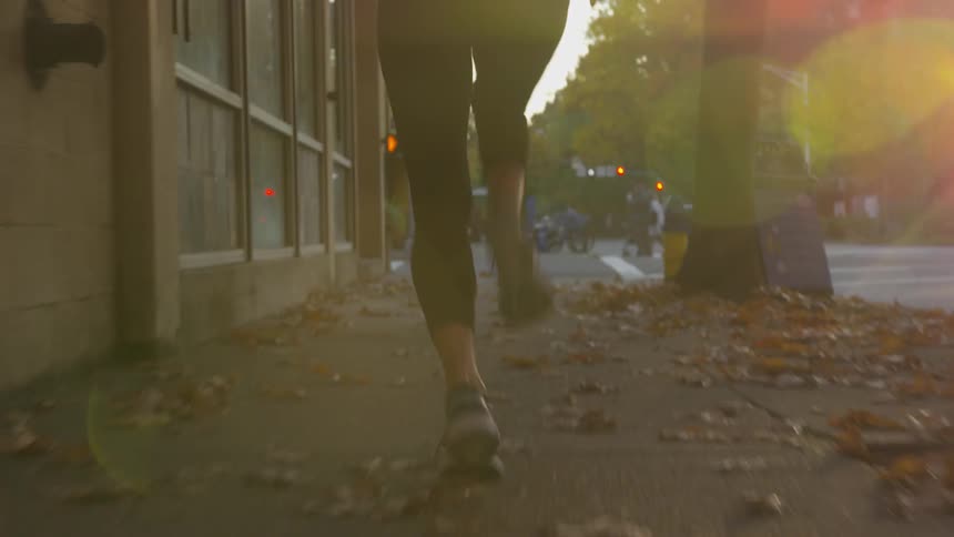 Woman wearing trainers runs over autumn leaves on the pavement in the city at dusk