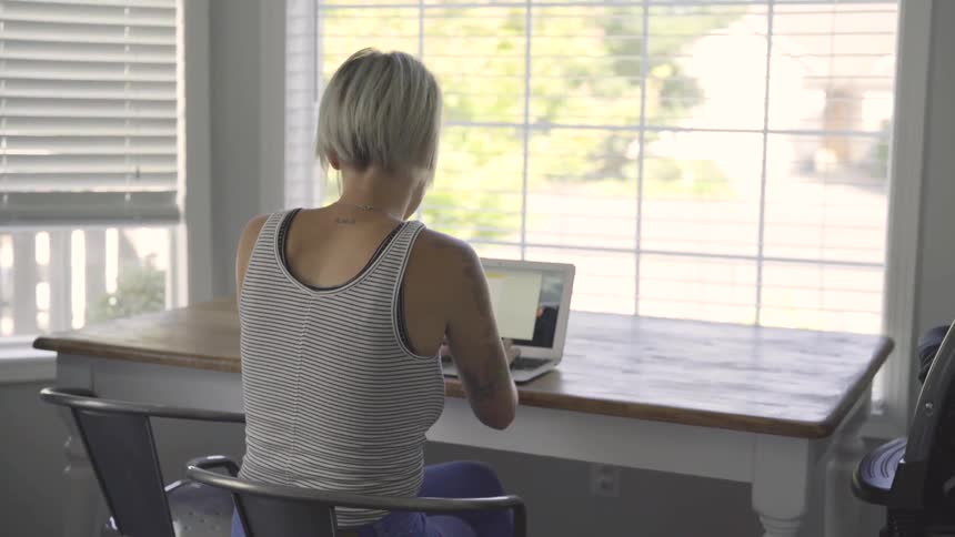 A young woman sits at a desk and types on her laptop