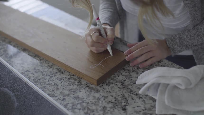 A woman writes on a wooden board with a white marker