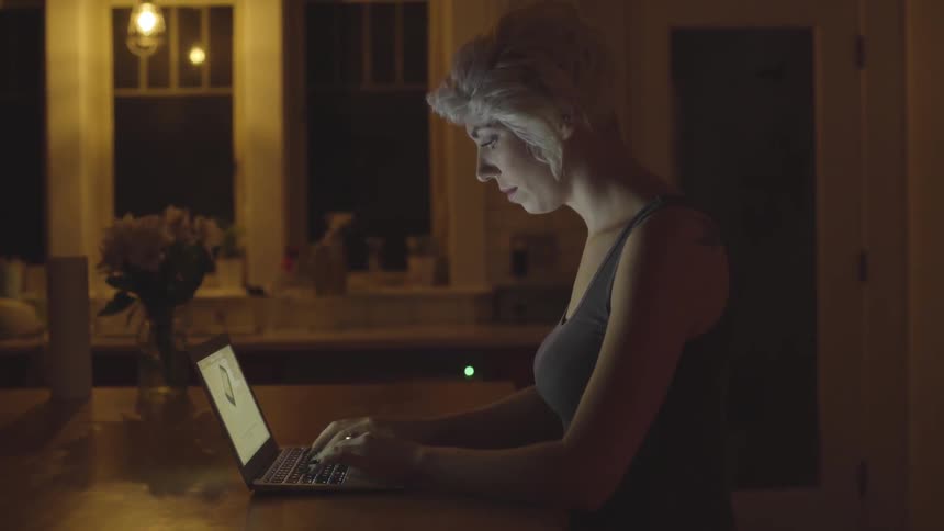 A woman types on a laptop in a kitchen at night