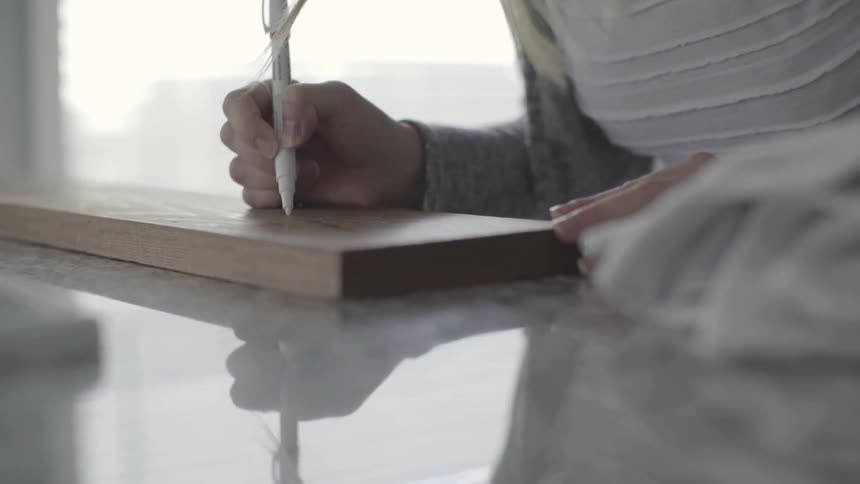 A blonde woman writes on a piece of wood