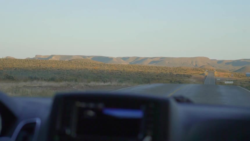 A car drives down a long road through grasslands