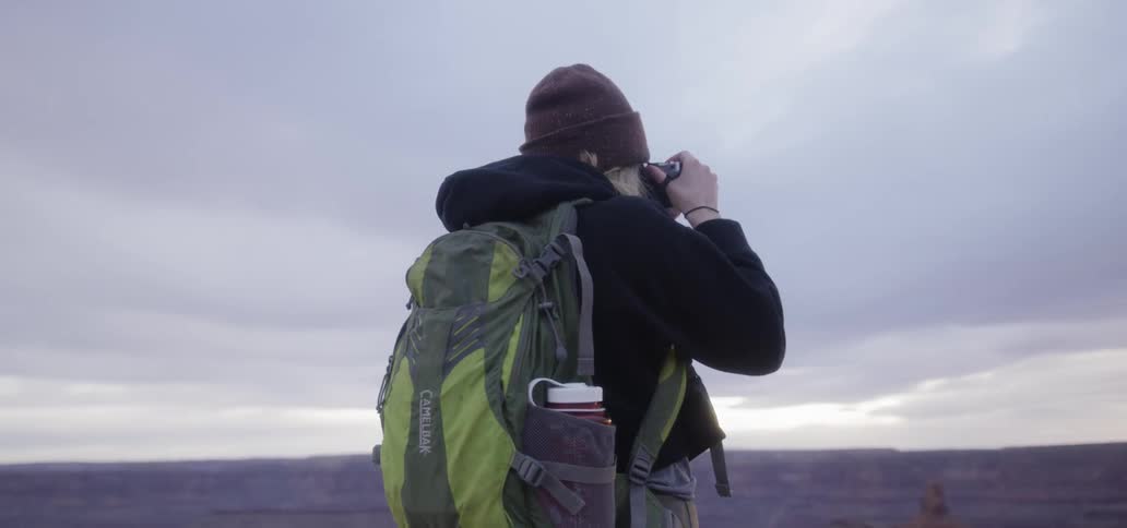 Woman in hiking gear taking photos on the top of a cliff at sunset