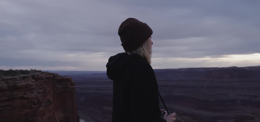 A white woman walks to the rim of a canyon and prepares to take a photograph with a camera