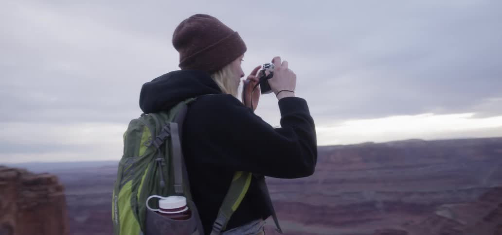 A woman is taking photographs on the cliff at sunset