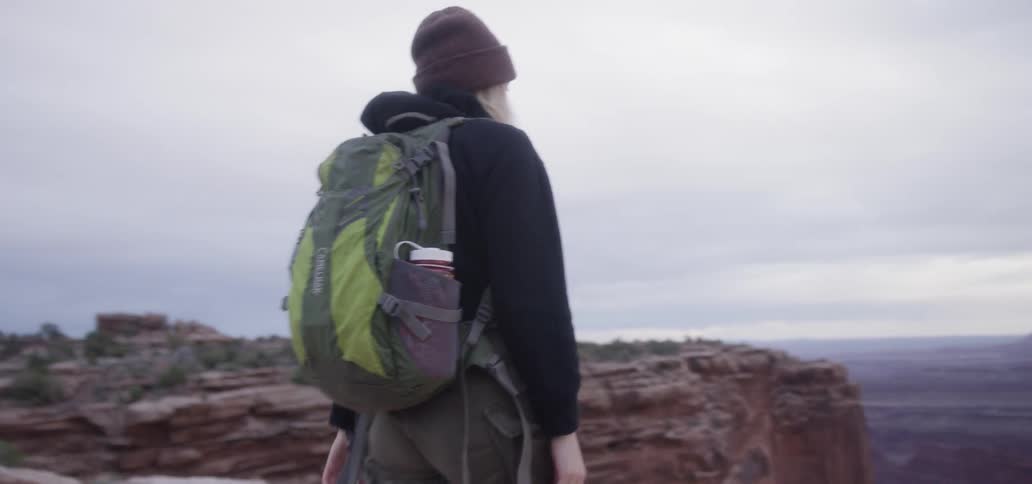 A woman walks to the edge of a cliff and raises her camera to her face