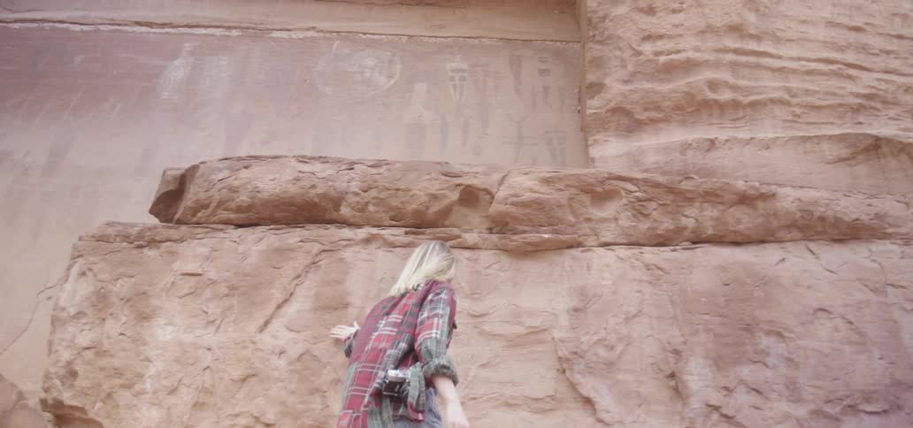 A woman is walking past a tall stone wall