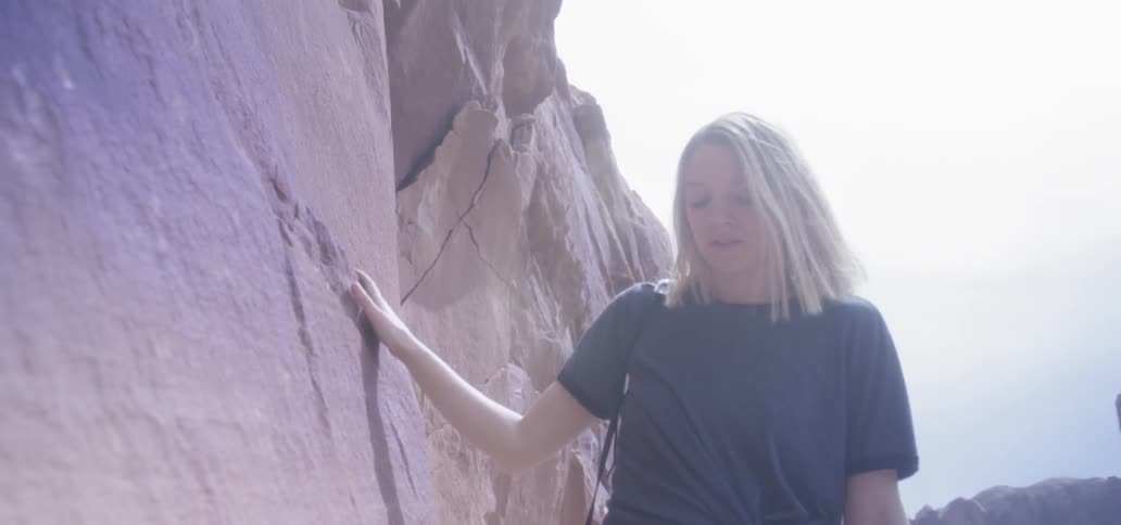 Woman runs hand across cliff rock