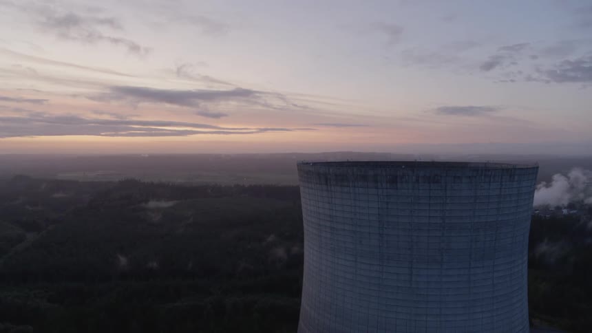 Ascending to the top of a tall power plant cooling tower surrounded by forest land at dusk