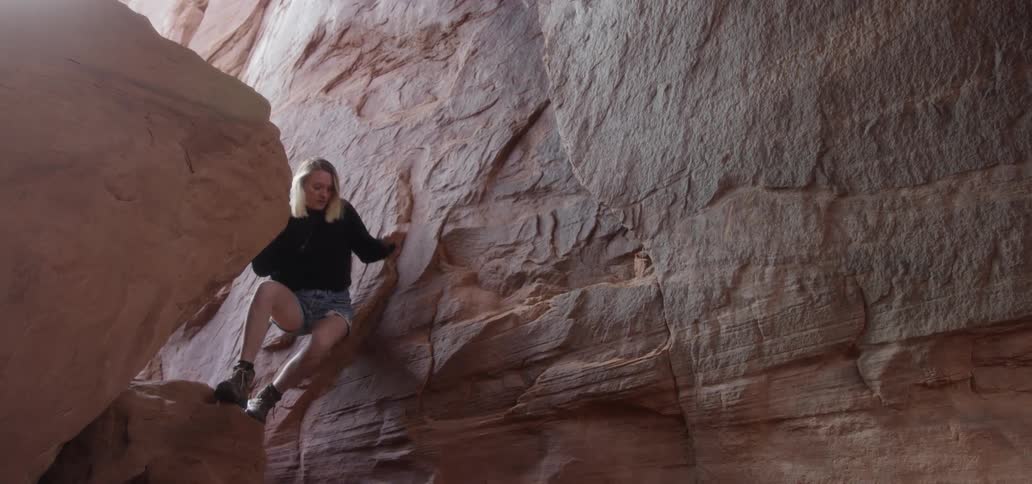 Woman climbs down from the large rock while holding to the wall