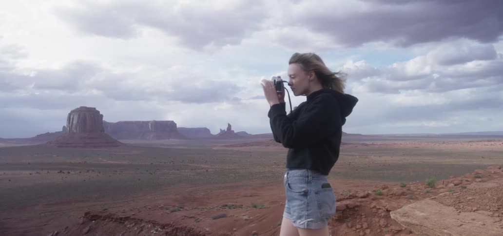 A young girls stands in a grassland and takes a picture