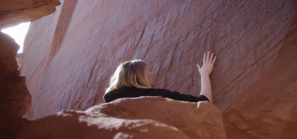 Woman runs hand along cliff wall