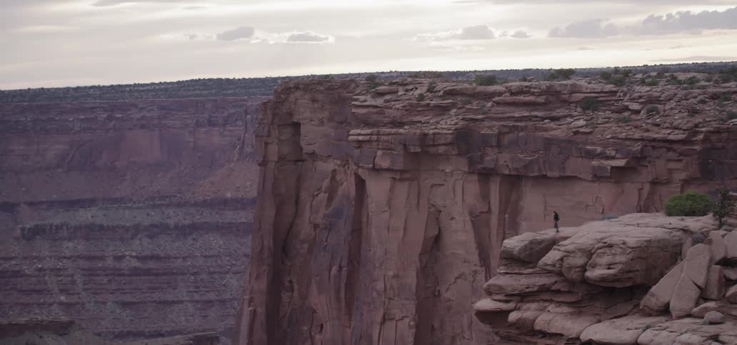 A person walks out onto a rocky ledge near striated cliffs
