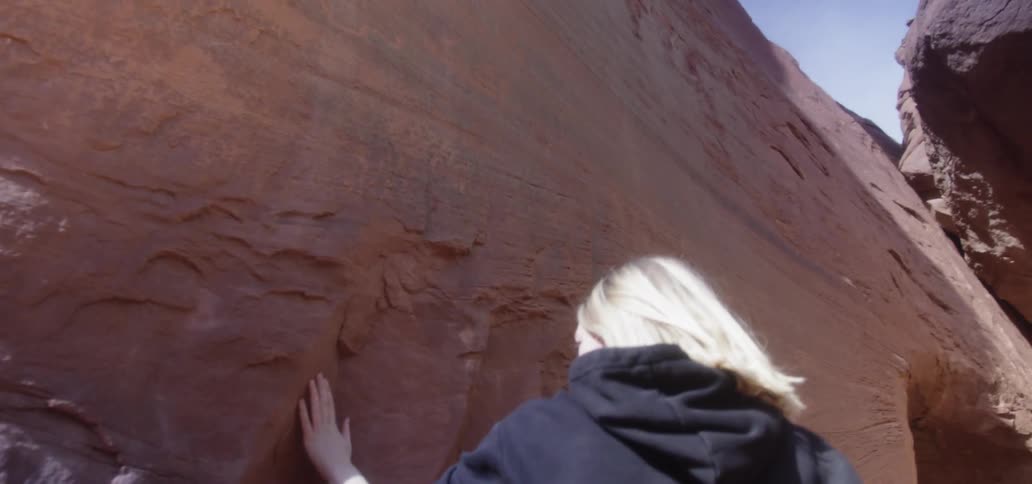A blonde white woman rubs her hand across a rock wall