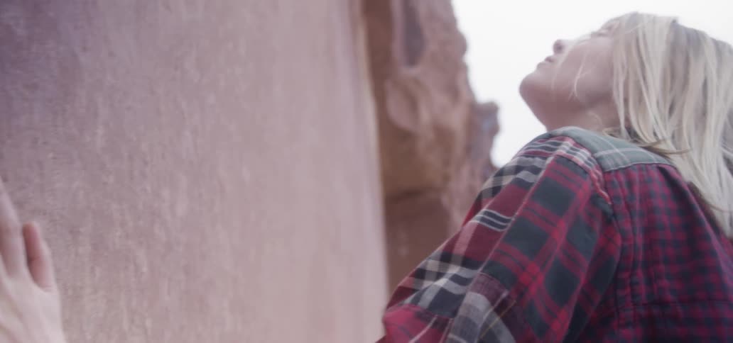 A woman in a red plaid shirt touching and examining an outdoor wall