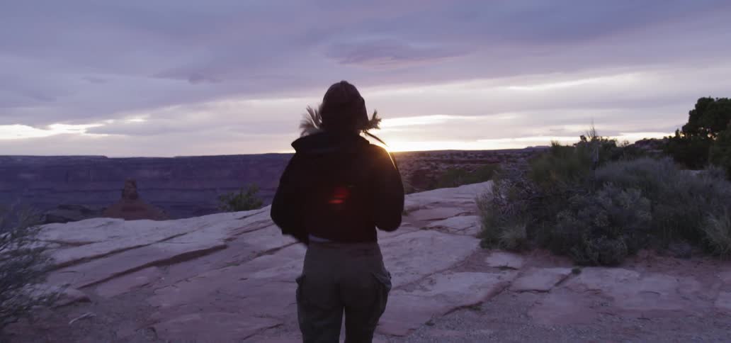 Woman runs towards desert cliff at sunset