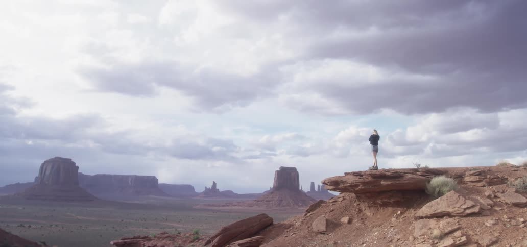 A woman takes a photograph while standing on a rock in a desert