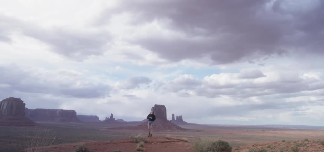 A young white woman stands in the middle of the desert taking a picture and then suddenly turns around