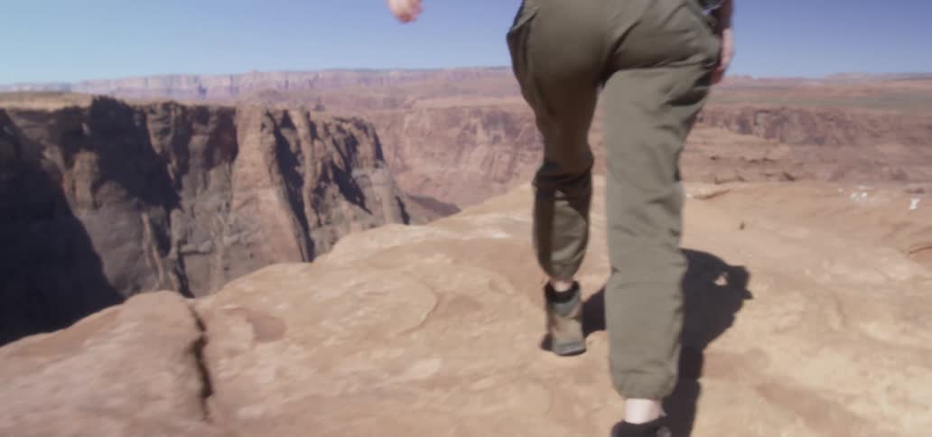 A young white woman climbs up to the top of a canyon cliff to take a picture