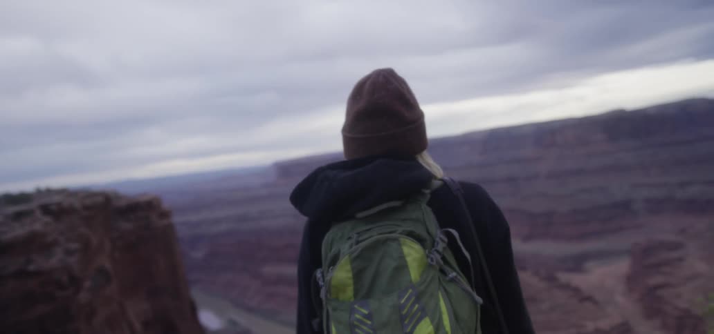 A white woman with a backpack walks to the rim of a canyon