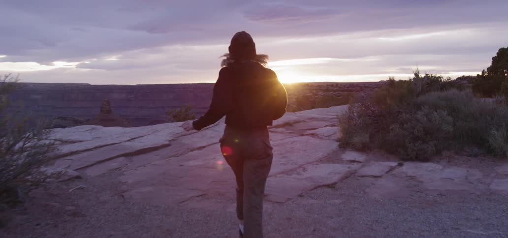 A person runs towards the edge of a cliff to view the sunset
