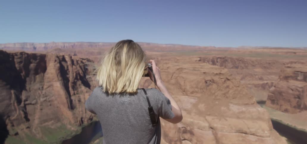 A woman takes a picture of a desert canyon