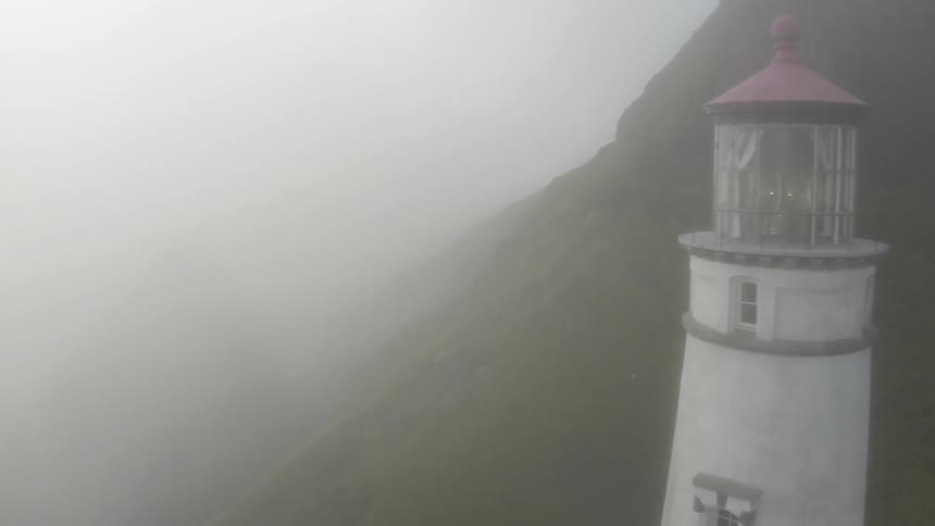 An aerial view of a lighthouse on a hillside on a foggy day
