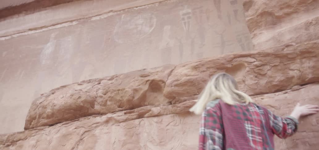 A woman rubs her hand along a large rock formation