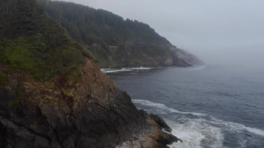 Ocean waves splash and break against the rocky coast on a foggy day