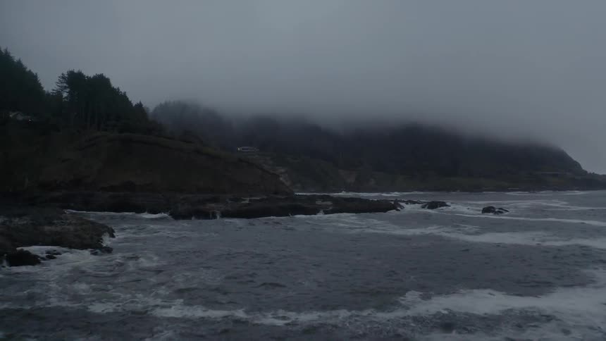 Ocean waves crash into a rocky shoreline on a misty day