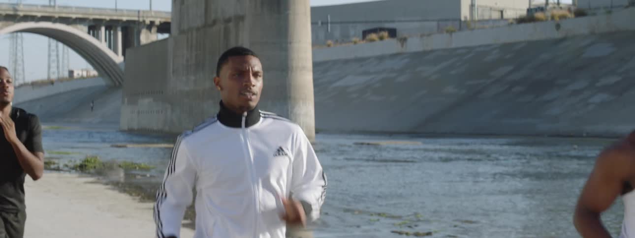 Three people are running by a canal near an overpass
