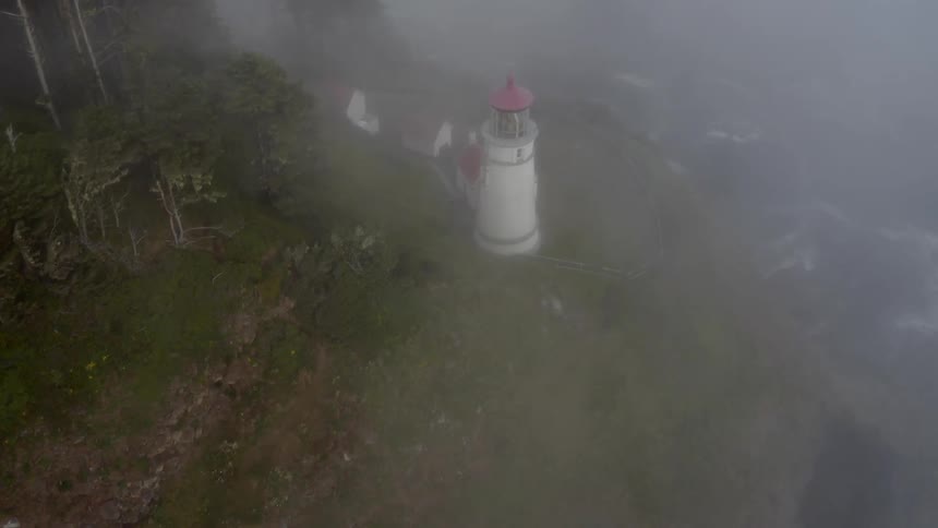 A lighthouse on a cliffs edge comes into view through the fog