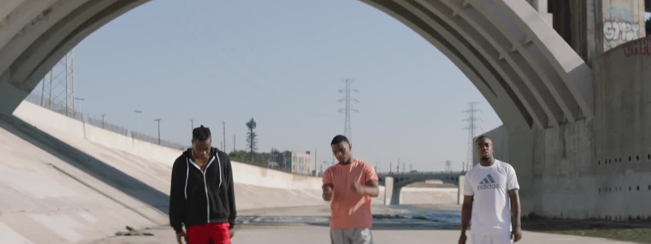 Three men are standing under a bridge in a straight line