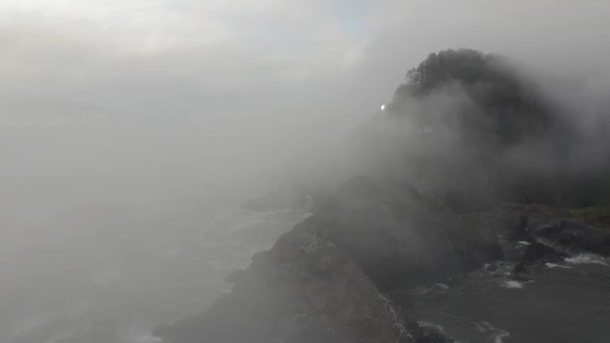 Thick fog is engulfing a rocky and forested coast line on a dreary day