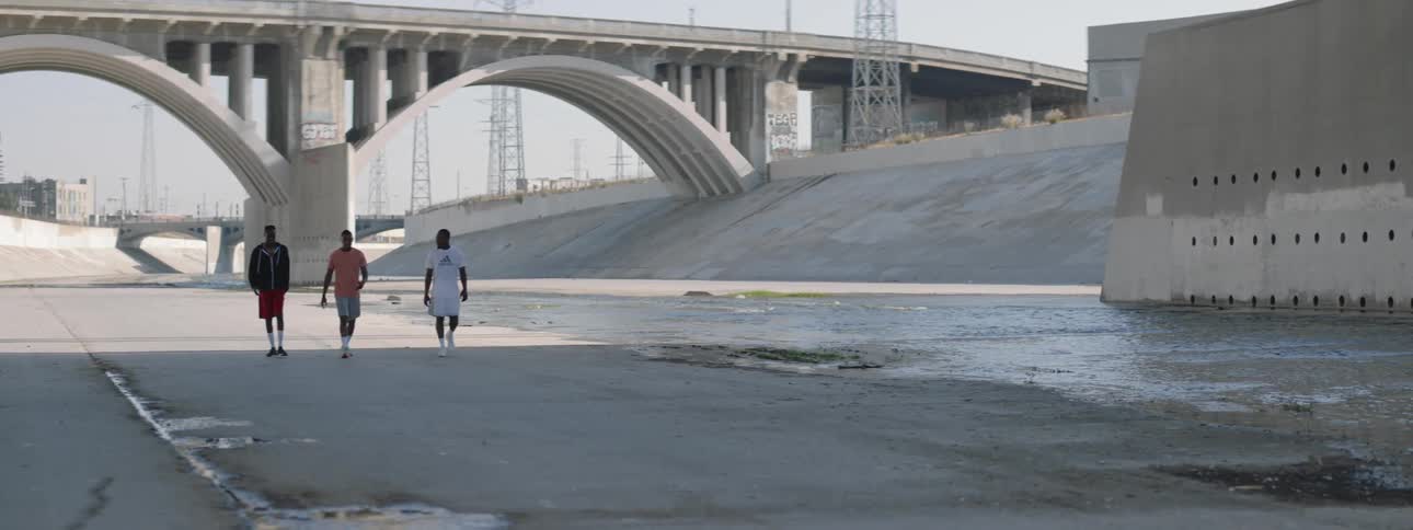 Three black males walk under the roadways in the concrete canals that are under los angeles