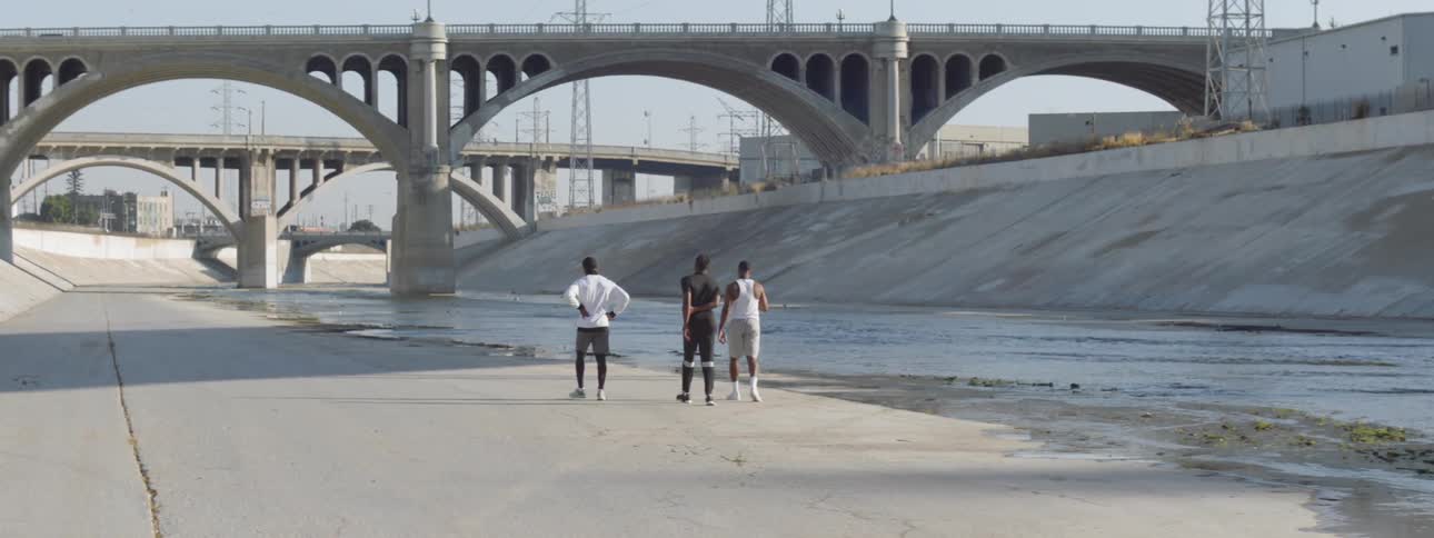 Three young black men walk along a viaduct towards a bridge