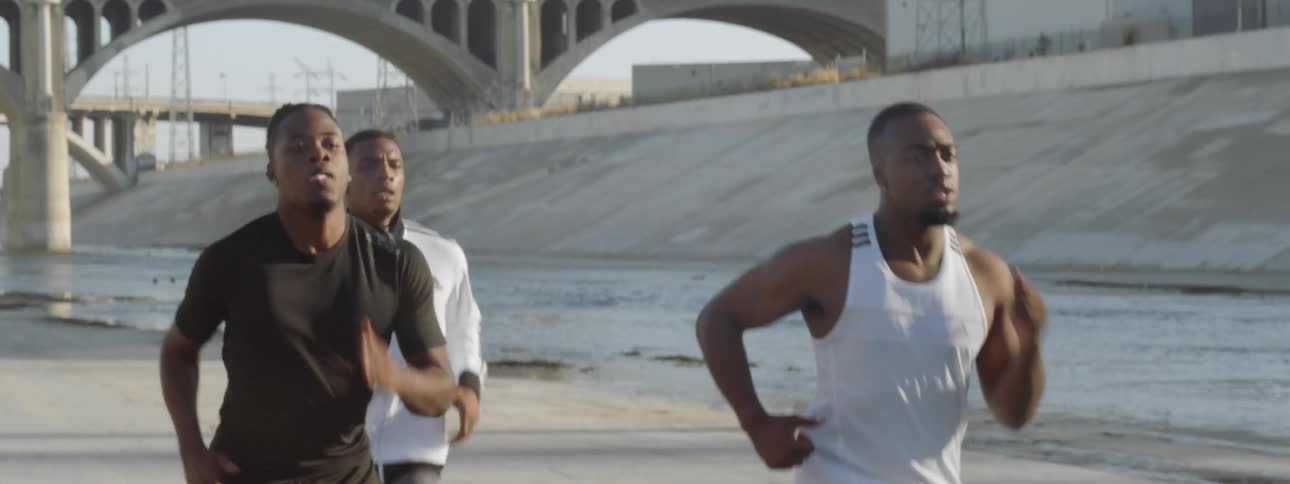Three black men running down a concrete floor control channel